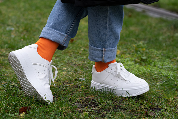 Frau steht mit weißen Halbschuhen auf einer Wiese und trägt orange gigando Socken