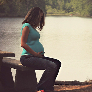 Schwangere Frau sitzt auf einer Steinbank. Unterstützt von den RS. Harmony Kompressions-Kniestrümpfen